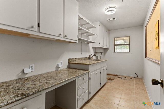 kitchen featuring light stone counters, a textured ceiling, sink, light tile patterned flooring, and white cabinetry