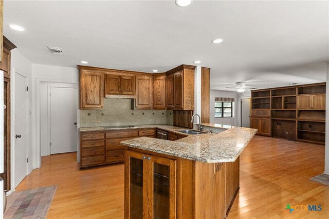 kitchen with sink, light stone counters, kitchen peninsula, backsplash, and light hardwood / wood-style flooring