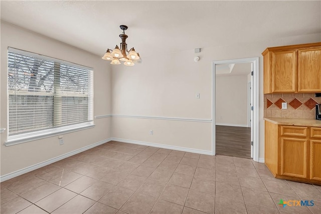 unfurnished dining area featuring a chandelier, light tile patterned floors, and baseboards