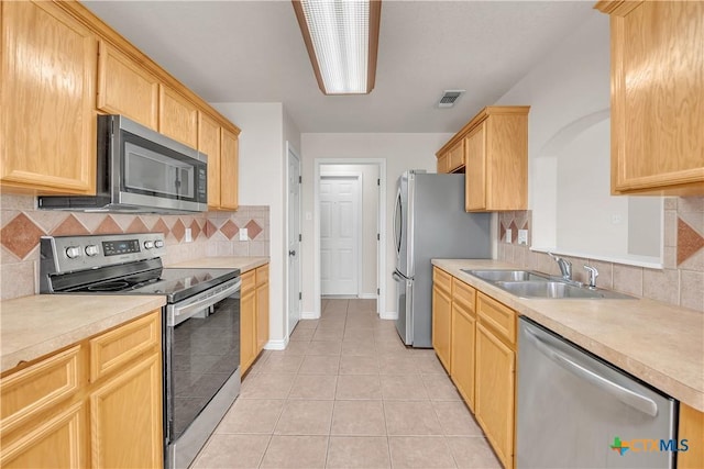 kitchen with light brown cabinetry, light countertops, light tile patterned floors, appliances with stainless steel finishes, and a sink