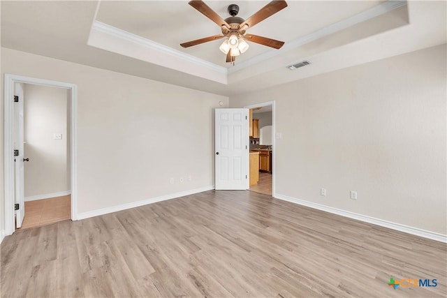 unfurnished room with a tray ceiling, light wood-style floors, visible vents, and ceiling fan