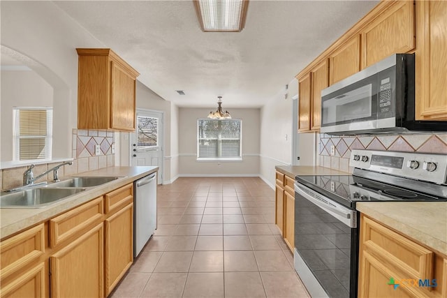 kitchen featuring light tile patterned flooring, a sink, stainless steel appliances, light countertops, and a notable chandelier