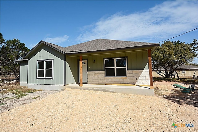 view of front of house featuring driveway, a shingled roof, stone siding, a porch, and board and batten siding