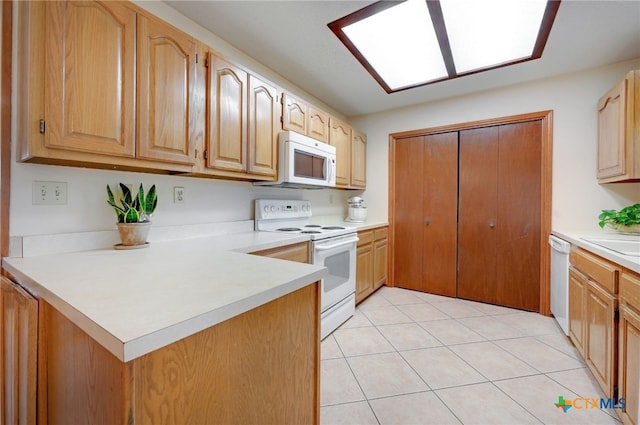 kitchen with light tile patterned floors, white appliances, a skylight, and kitchen peninsula