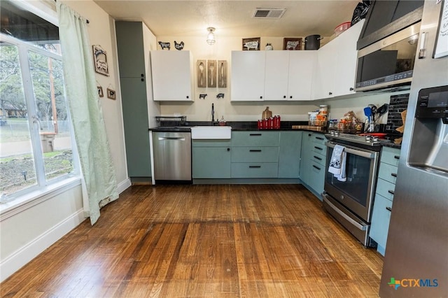 kitchen with stainless steel appliances, dark countertops, visible vents, white cabinetry, and a sink