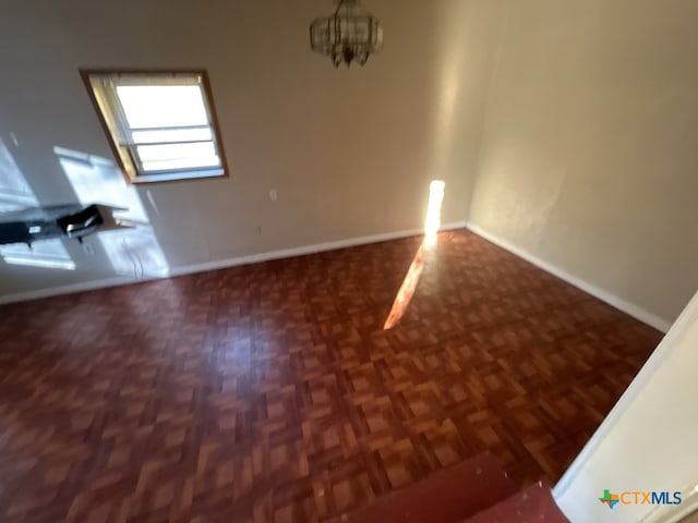 empty room featuring dark parquet flooring and an inviting chandelier