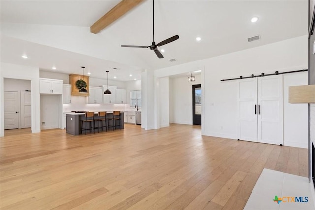 unfurnished living room with lofted ceiling with beams, recessed lighting, ceiling fan, light wood-style floors, and a barn door