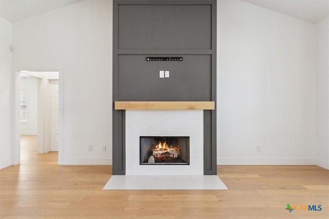 unfurnished living room featuring vaulted ceiling, a fireplace, baseboards, and wood finished floors