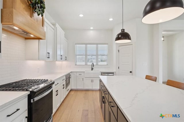 kitchen with premium range hood, light wood-type flooring, a sink, range with gas stovetop, and decorative backsplash