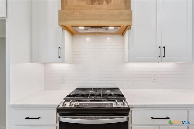 kitchen featuring tasteful backsplash, stainless steel range with gas cooktop, premium range hood, light stone counters, and white cabinetry