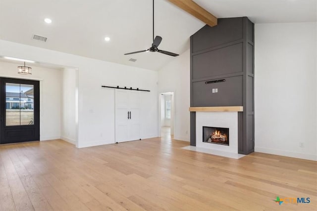 unfurnished living room featuring visible vents, a large fireplace, a barn door, beam ceiling, and light wood-style floors