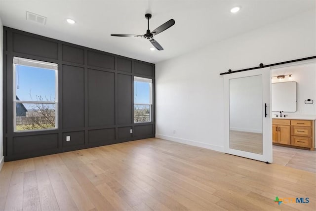 unfurnished bedroom featuring visible vents, light wood-style floors, a barn door, a decorative wall, and multiple windows