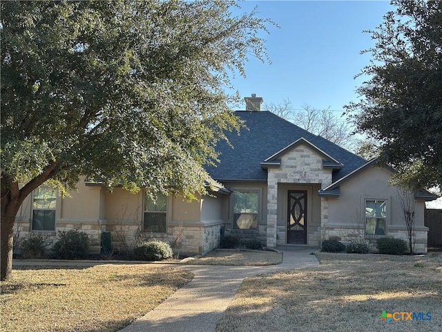 view of front of home featuring stone siding, a front lawn, roof with shingles, and stucco siding