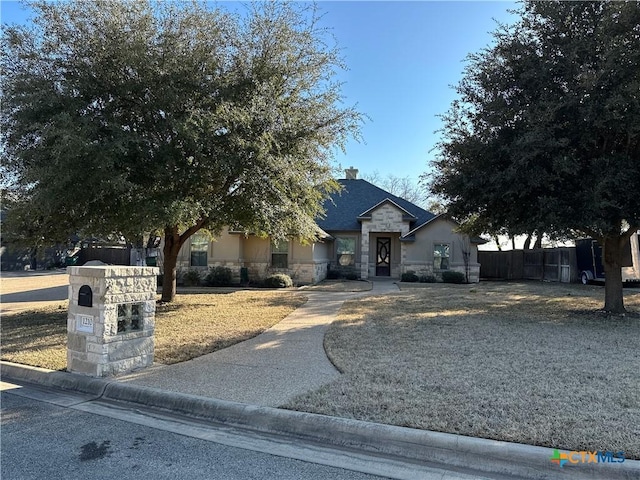 view of front of property with stone siding, fence, and stucco siding