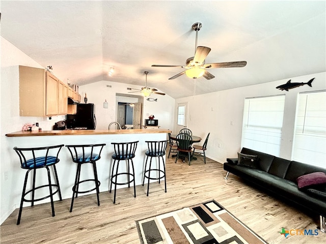 kitchen with light brown cabinetry, lofted ceiling, a breakfast bar, and light hardwood / wood-style flooring