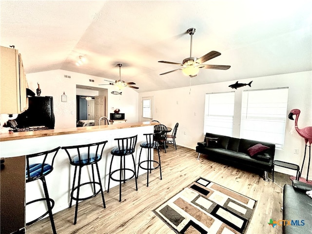 living room with light hardwood / wood-style floors, sink, ceiling fan, and vaulted ceiling