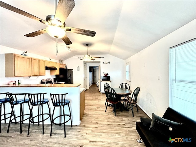 kitchen with black fridge, lofted ceiling, a breakfast bar, light wood-type flooring, and light brown cabinetry