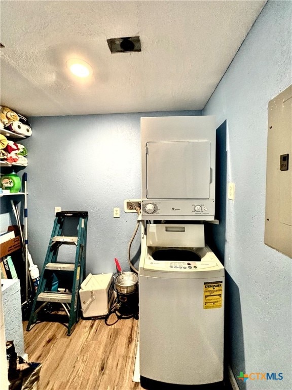 laundry room featuring electric panel, a textured ceiling, stacked washer and dryer, and light hardwood / wood-style flooring