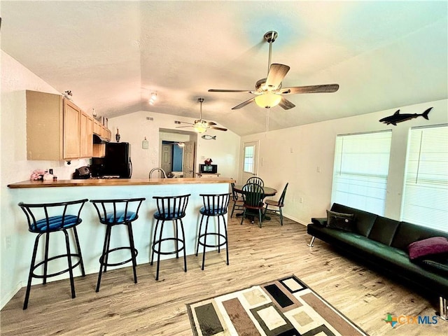 101 N 13th St, Seadrift, TX 77983 - kitchen with light wood finished floors, vaulted ceiling, a peninsula, a breakfast bar, and freestanding refrigerator