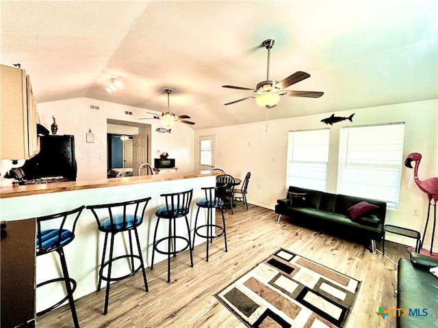 kitchen with light hardwood / wood-style floors, lofted ceiling, black refrigerator, a breakfast bar area, and sink