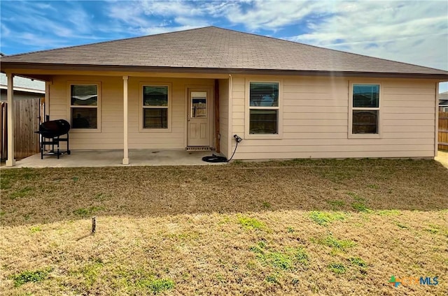 rear view of property with a shingled roof, a patio area, fence, and a lawn