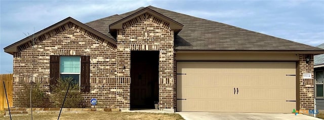 french country inspired facade with brick siding, a shingled roof, concrete driveway, an attached garage, and fence