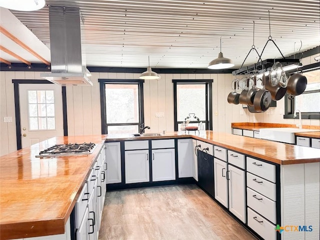 kitchen featuring island range hood, wood counters, white cabinetry, sink, and stainless steel gas cooktop