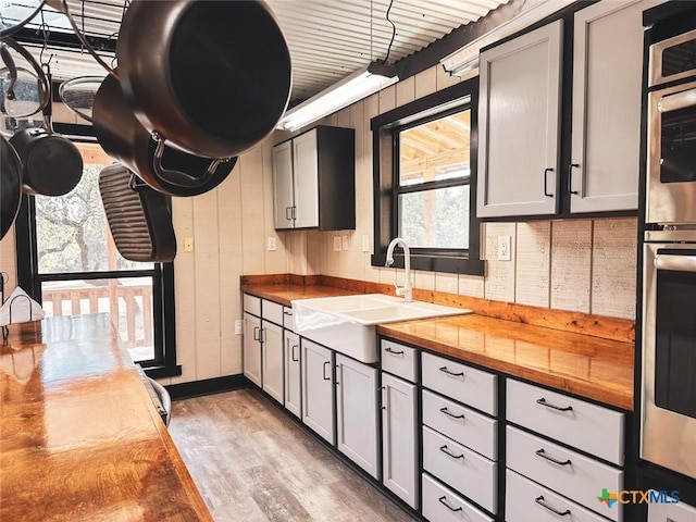 kitchen with butcher block counters, sink, light hardwood / wood-style flooring, and gray cabinetry