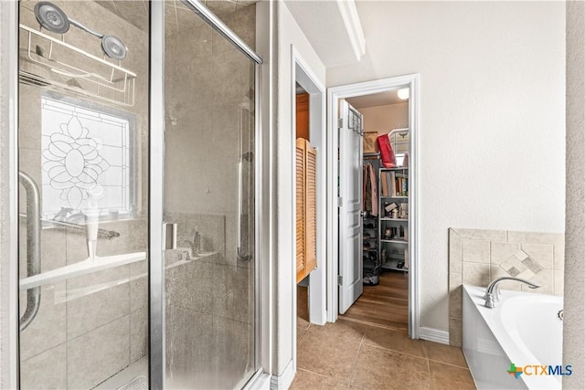 full bath featuring a garden tub, a shower stall, a walk in closet, and tile patterned flooring