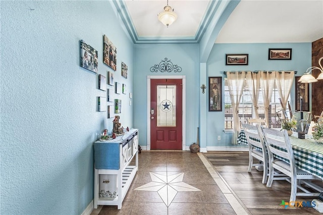 tiled entrance foyer with arched walkways, a textured wall, and baseboards