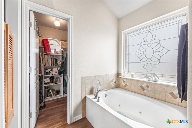 full bathroom featuring a spacious closet, a tub with jets, and wood finished floors