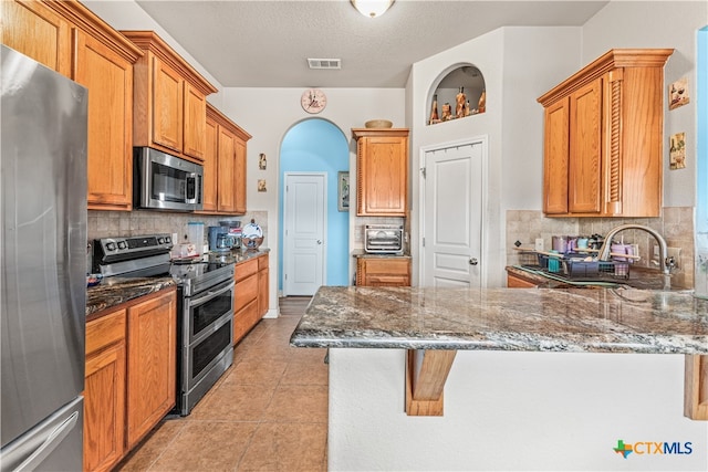 kitchen featuring light tile patterned flooring, stainless steel appliances, a peninsula, visible vents, and dark stone counters