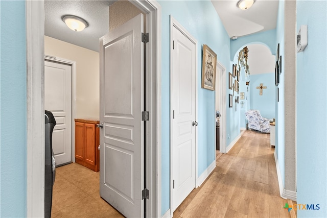 corridor featuring light wood-type flooring, baseboards, arched walkways, and a textured ceiling