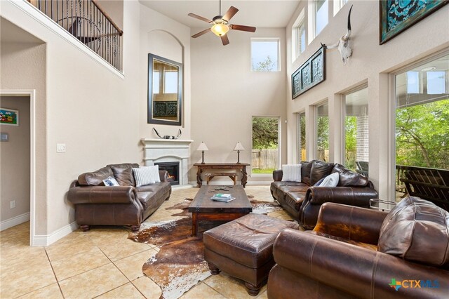 618 Oak Brook Dr, New Braunfels, TX 78132 - living room featuring a high ceiling, ceiling fan, a warm lit fireplace, baseboards, and light tile patterned floors
