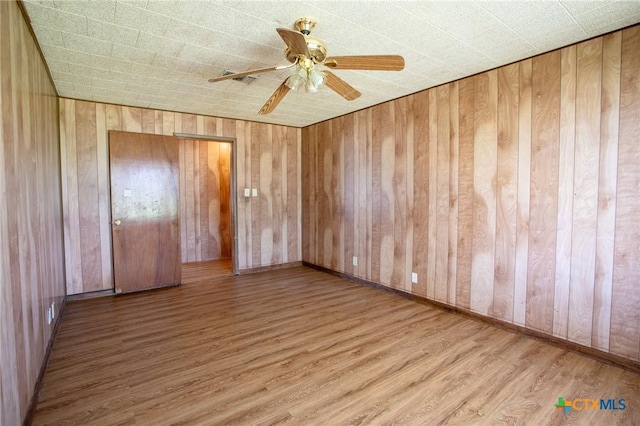 unfurnished bedroom with hardwood / wood-style flooring, ceiling fan, and wood walls