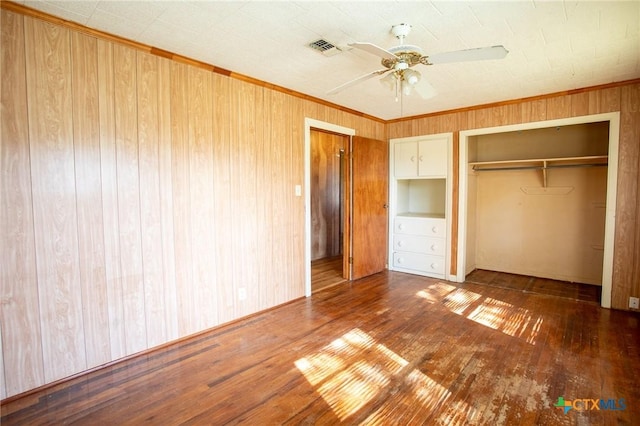 unfurnished bedroom featuring crown molding, hardwood / wood-style floors, wooden walls, and a closet