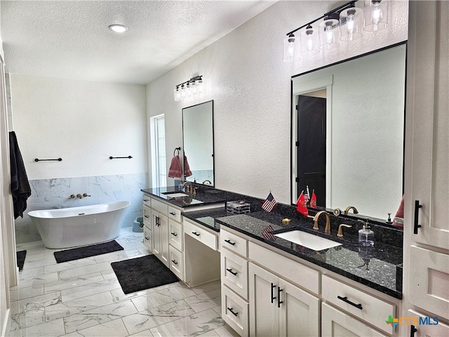 bathroom featuring a textured ceiling, vanity, a bath, and tile walls