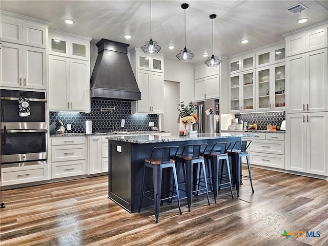 kitchen featuring custom exhaust hood, a center island with sink, white cabinets, hardwood / wood-style flooring, and stainless steel appliances