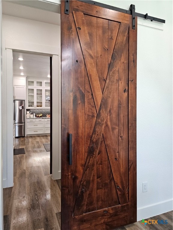 details with decorative backsplash, a barn door, wood-type flooring, and stainless steel refrigerator