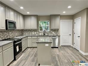 kitchen featuring sink, a center island, decorative backsplash, appliances with stainless steel finishes, and light wood-type flooring