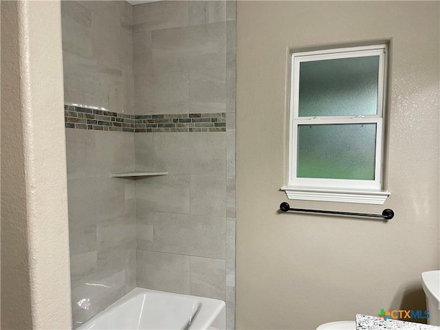 bathroom with toilet and tiled shower / bath