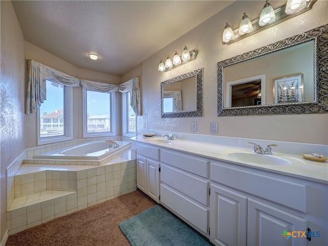 bathroom featuring a relaxing tiled tub, vanity, and a textured ceiling