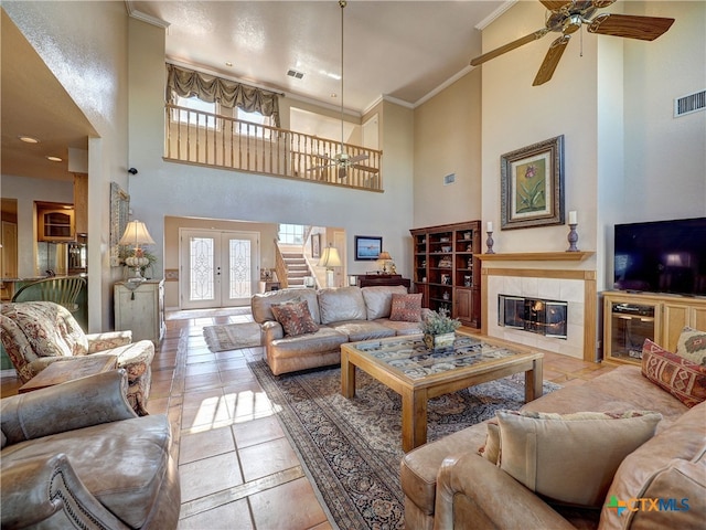 living room featuring french doors, ceiling fan, a tile fireplace, and a high ceiling