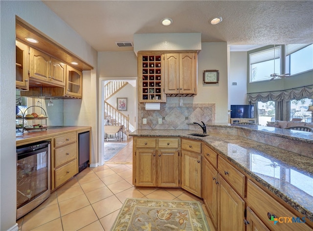 kitchen with beverage cooler, backsplash, light tile patterned floors, kitchen peninsula, and light stone countertops