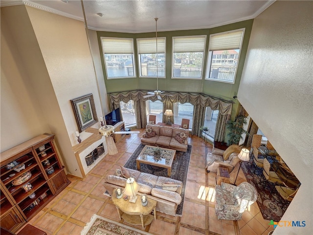 tiled living room featuring crown molding, ceiling fan, a high ceiling, and a wealth of natural light