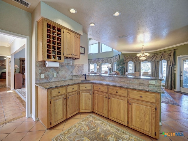 kitchen with backsplash, light stone counters, a notable chandelier, light tile patterned flooring, and kitchen peninsula