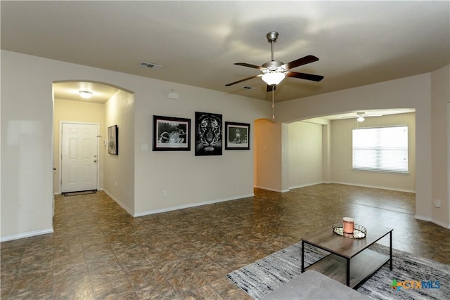 unfurnished living room featuring baseboards, arched walkways, a ceiling fan, and visible vents