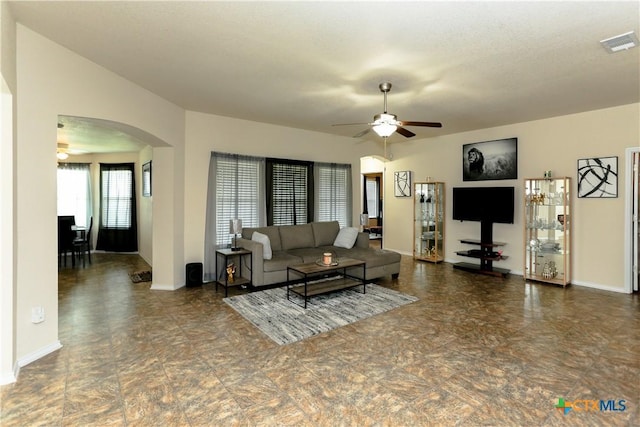 living room with arched walkways, baseboards, visible vents, and ceiling fan