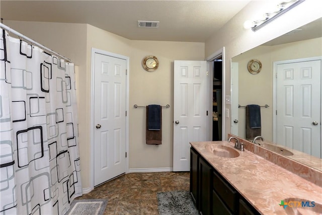 full bath with baseboards, visible vents, a sink, curtained shower, and double vanity