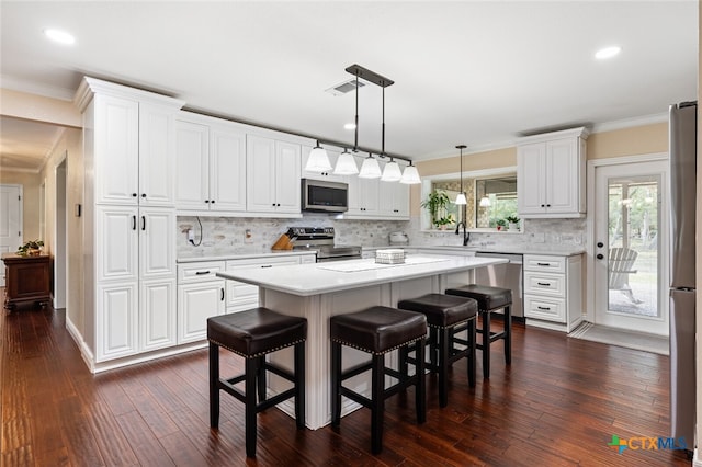 kitchen with stainless steel appliances, a kitchen breakfast bar, a center island, white cabinets, and dark wood-type flooring